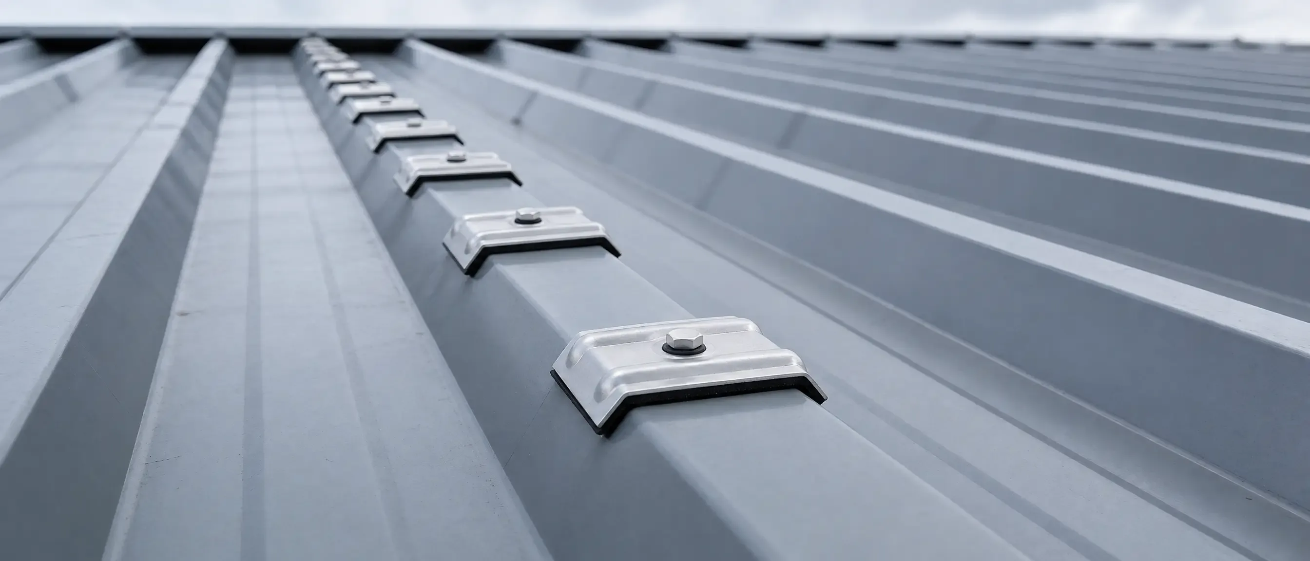 Reihe verschraubter Kalotten aus Aluminium auf der Obergurt-Rippe eines Trapezblechdachs