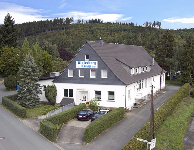 Luftbild des Firmensitzes der Winterberg & Knapp GmbH mit Schriftzug am Haus, davor Parkplatz und Bäume